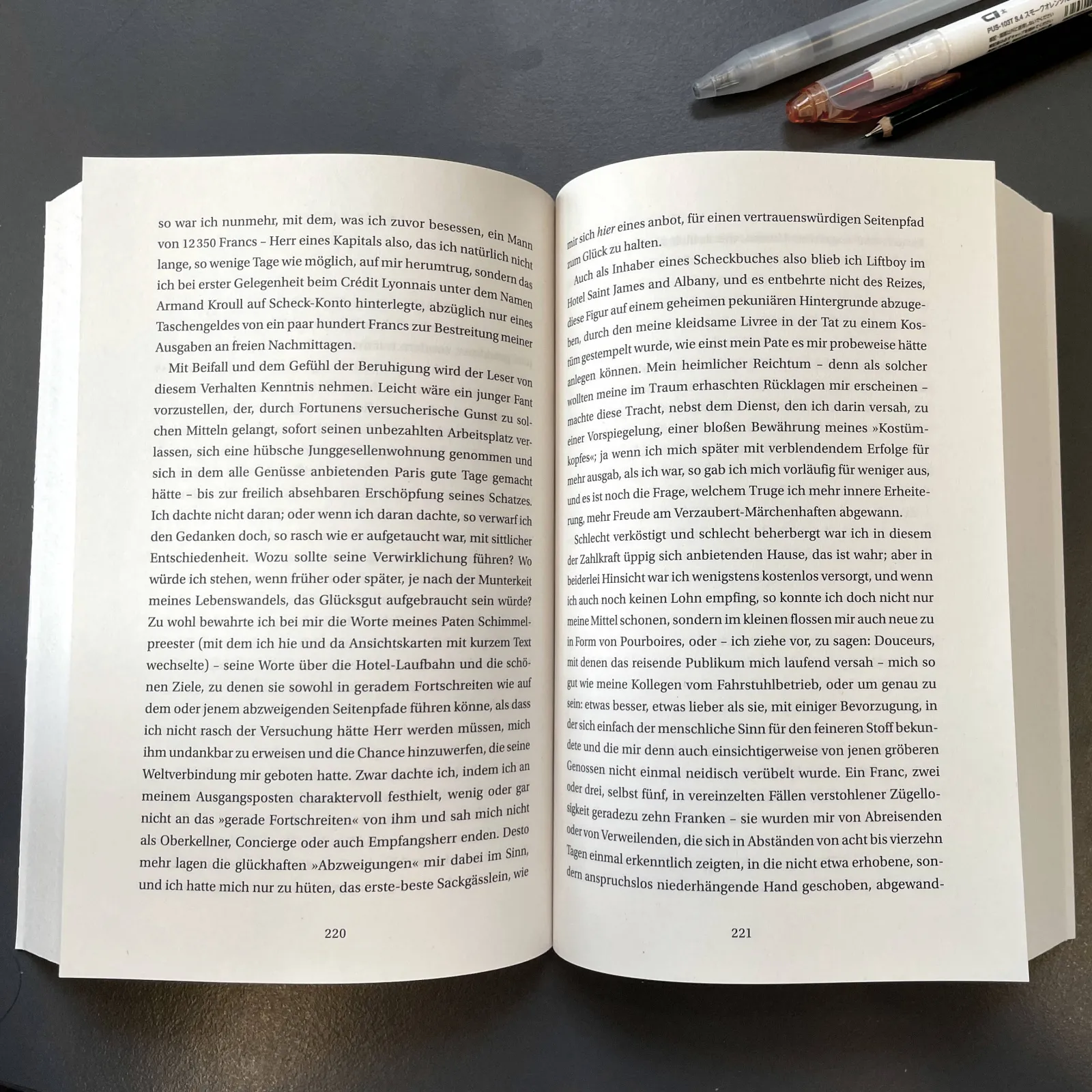 An open book on a desk, with marker pens beside it.